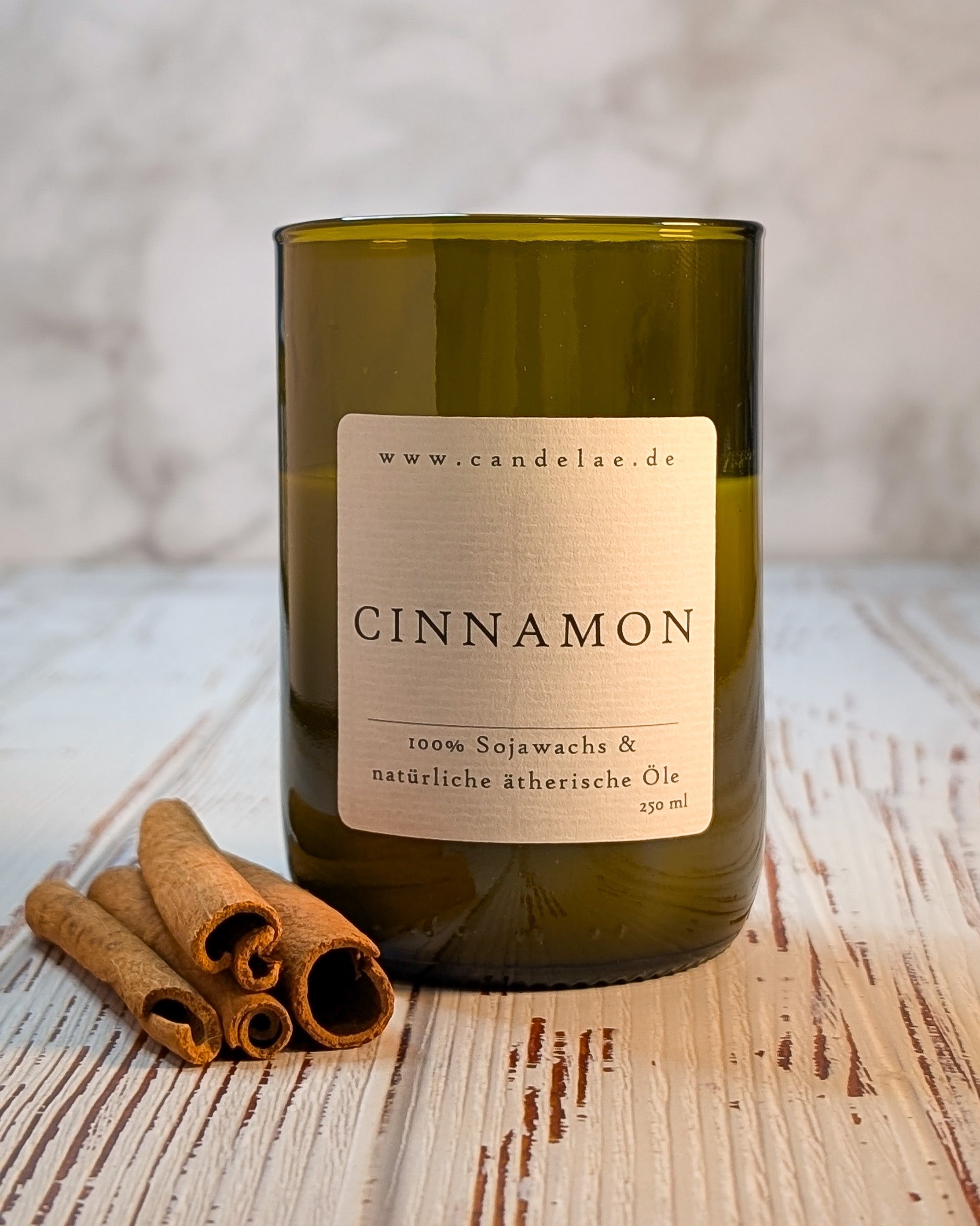 Zimt-Duftkerze aus Sojawachs im upgecycelten Weinflaschen-Glas (250 ml) von Candelae – mit Zimtstangen, Moodfoto auf Holz.