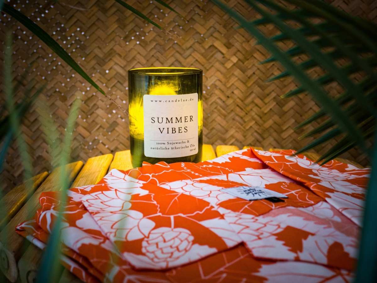 Duftkerze Summer Vibes und buntes Hawaiihemd symbolisieren sommerliche Düfte und fröhliche Stimmung
