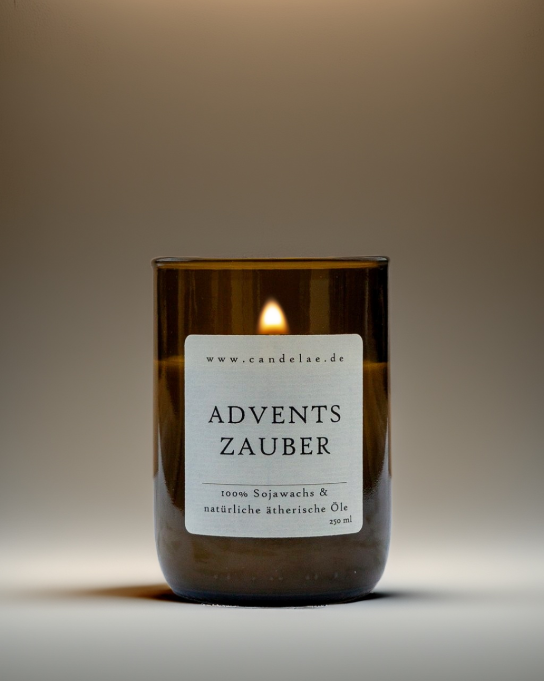 Adventszauber Duftkerze von Candelae – brennende vegane Sojawachs-Kerze, 250 ml, in recycelter Weinflasche mit natürlichen ätherischen Ölen vor warmem Studiohintergrund.