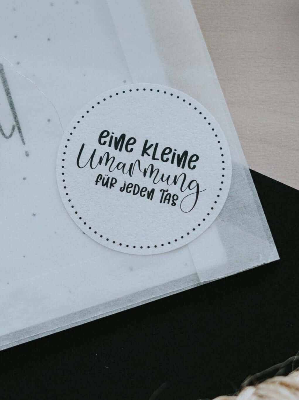 Weißer runder Sticker mit dem Spruch „Eine kleine Umarmung für jeden Tag“ für Geschenke und Karten