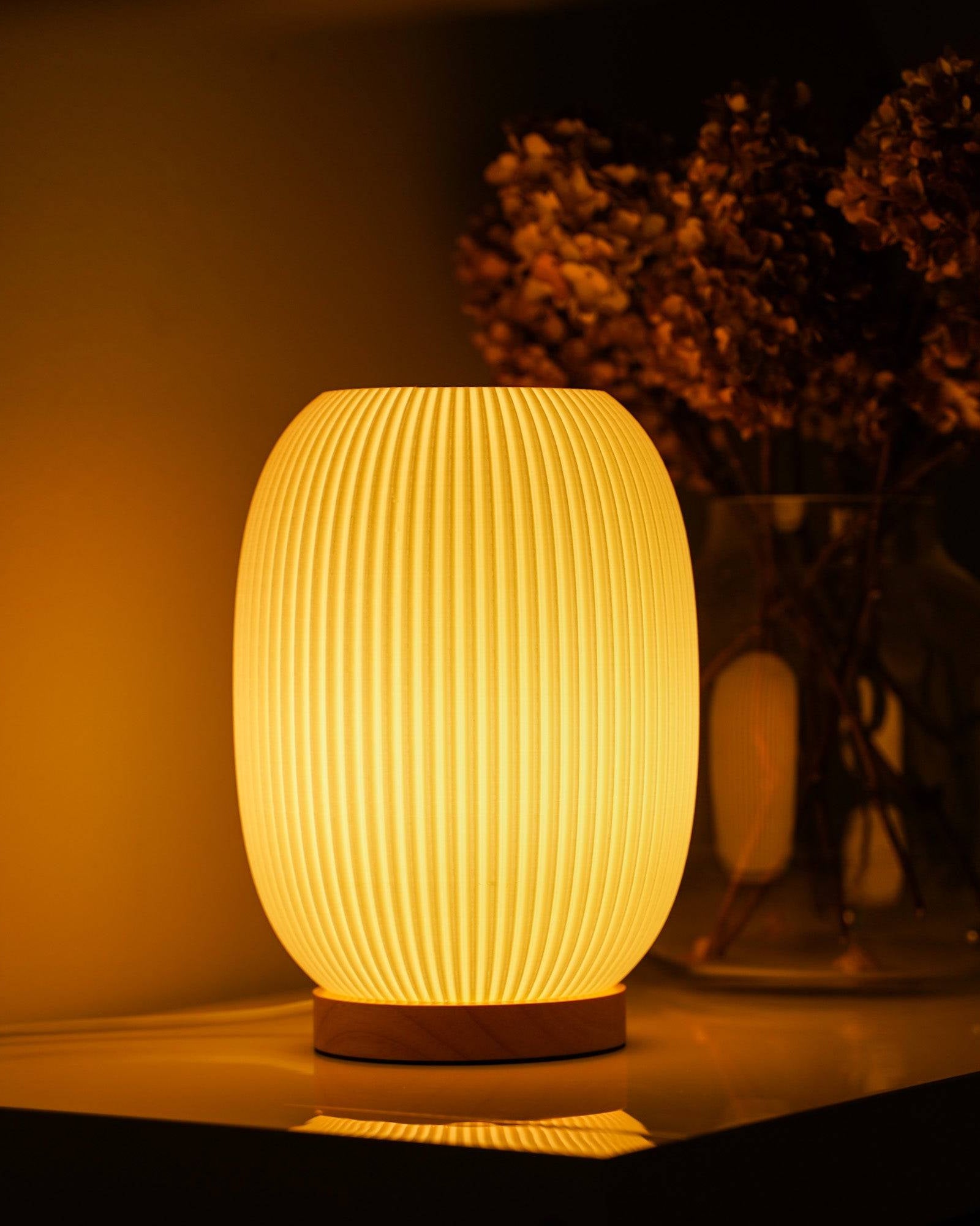Moonou Boa 3D-gedruckte Tischlampe aus PLA mit Rillenstruktur und Eichenholz-Sockel, warmes Licht auf dem Sideboard neben Glasvase