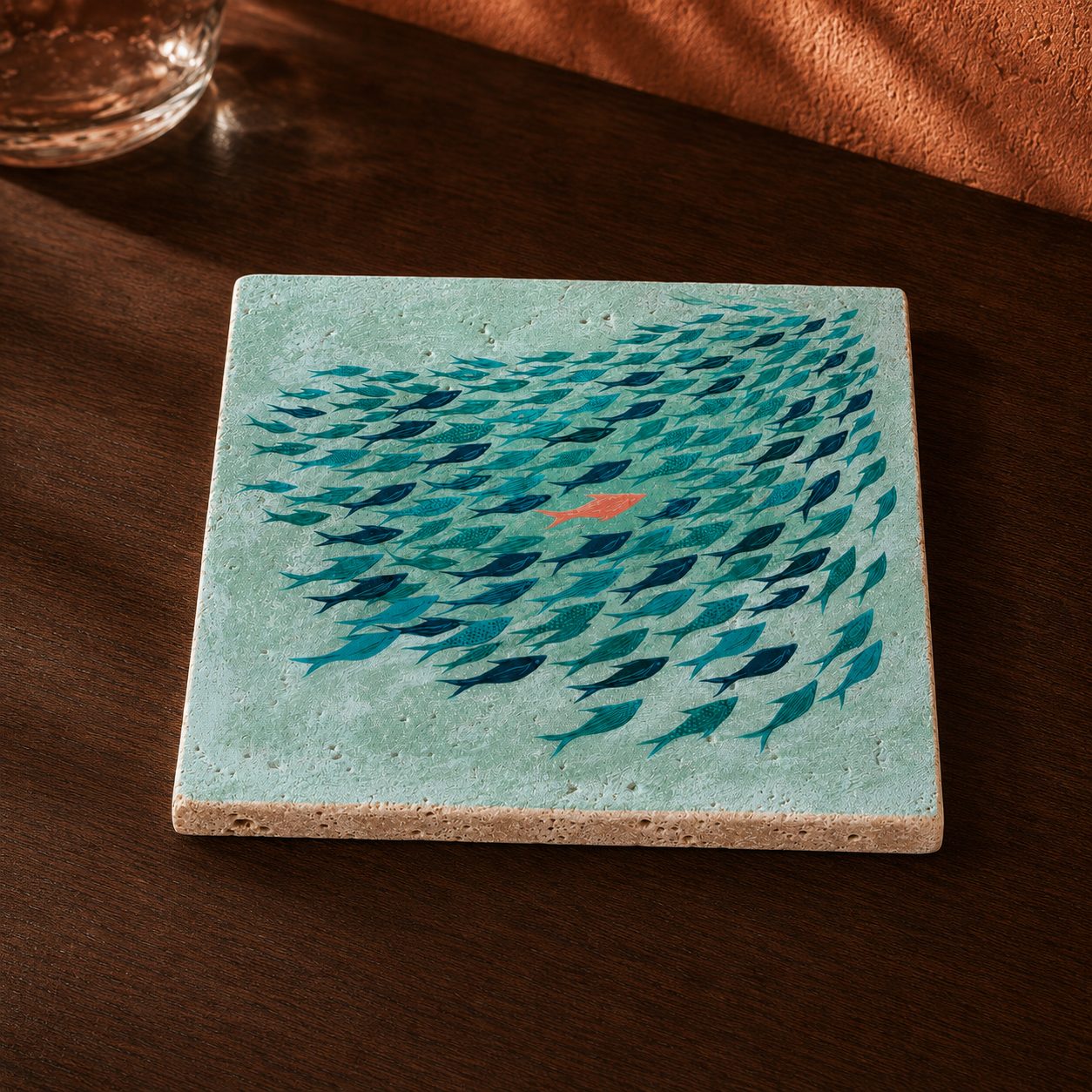 Kleines Kunstwerk aus Travertin „Gegen den Strom“ mit blau-türkisem Fischschwarm und korallrotem Fisch auf einem dunklen Holztisch.