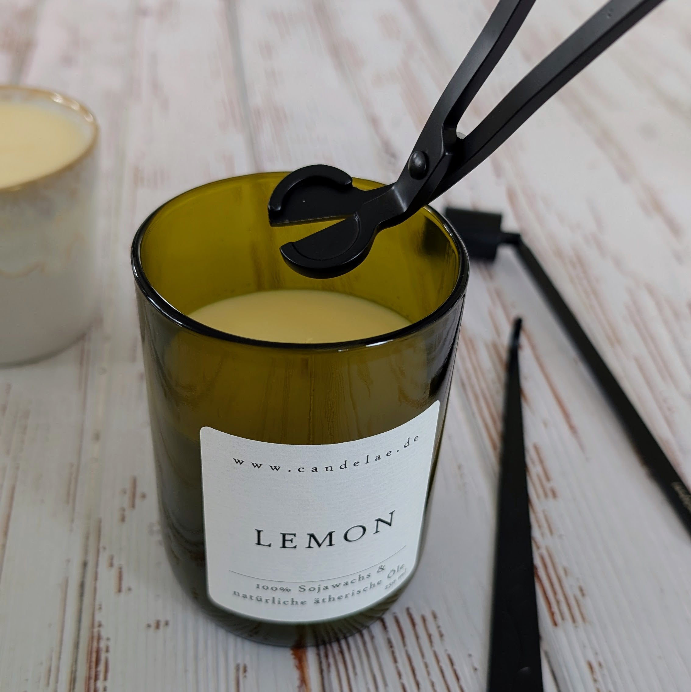Kerzenpflege mit Dochtschere – Candelae Duftkerze ‚Lemon‘ im recycelten Weinflaschenglas beim Kürzen des Dochtes, Kerzenpflege-Set Schwarz