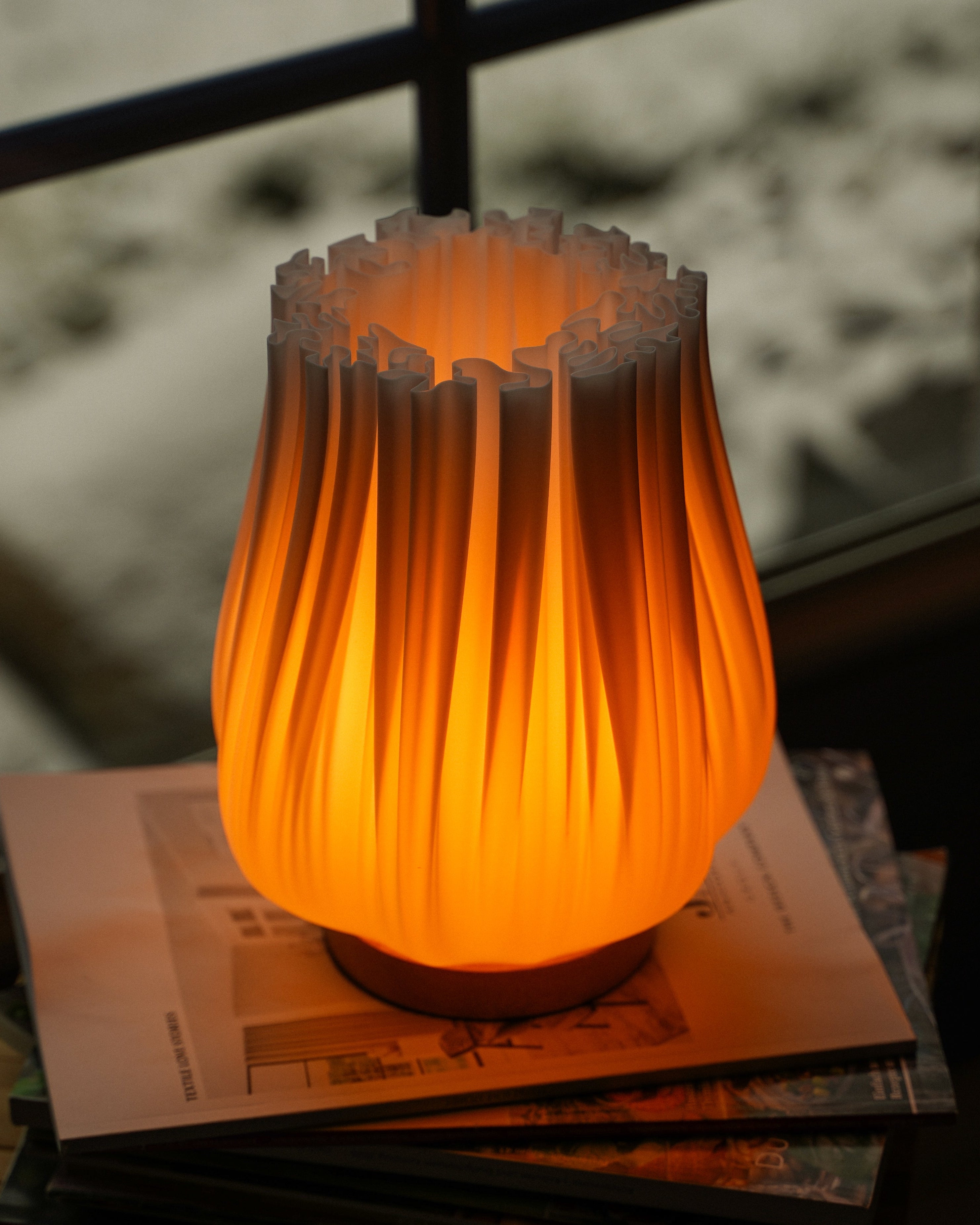 Moonou ‚Cora‘ – 3D-gedruckte Falten-Tischlampe mit warmweißem 2100 K Licht, auf Magazinen am Fenster; PLA-Schirm, Eichenholz-Sockel, E27, dimmbar