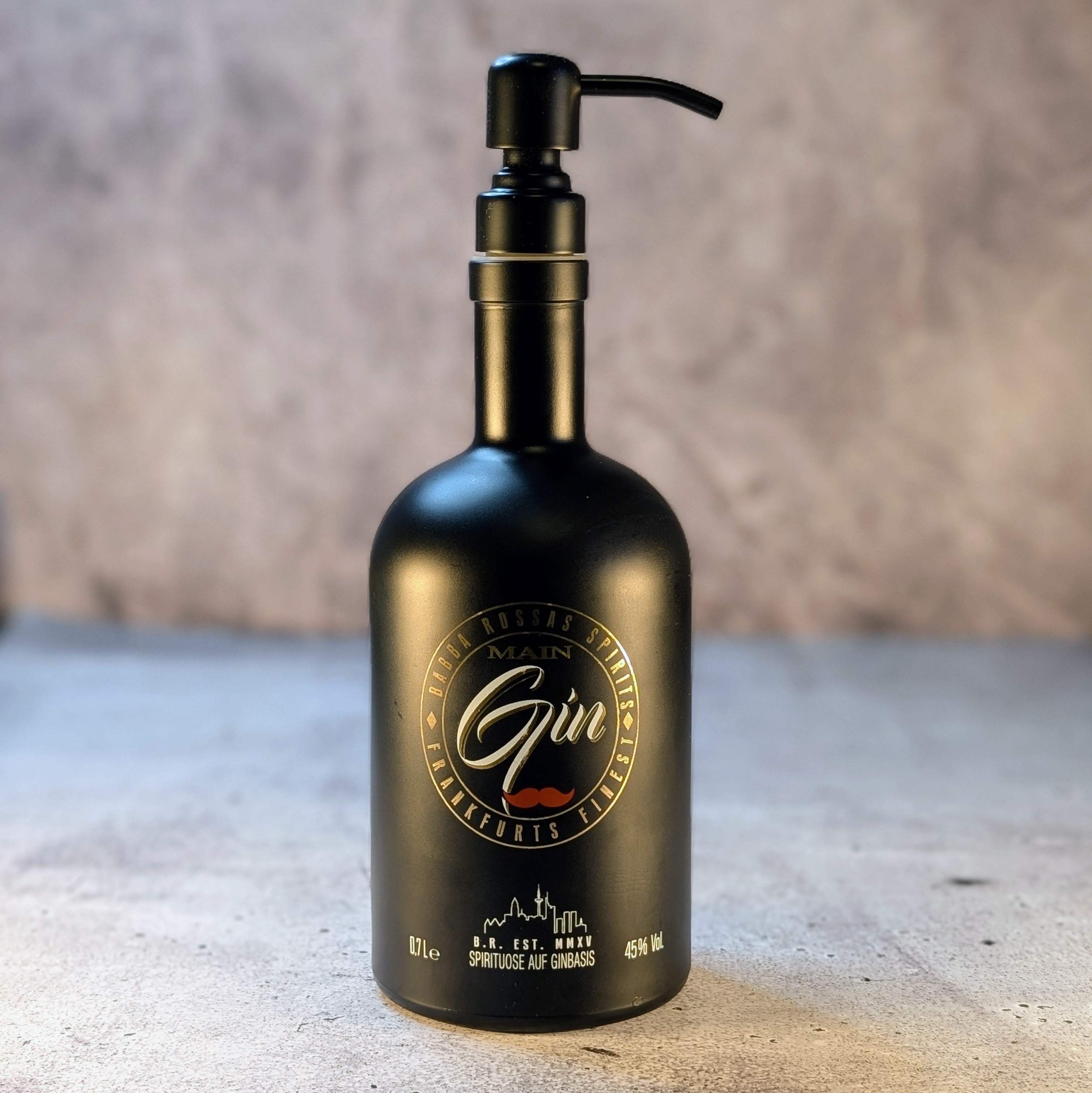 Seifenspender aus einer recycelten "Main Gin"-Flasche mit Pumpenkopf in mattem Schwarz, elegant auf einer hellen Steinoberfläche abgelichtet.