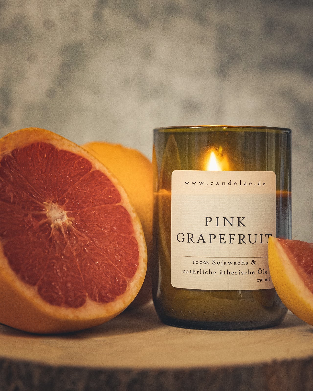 Duftkerze Pink Grapefruit aus Sojawachs in einem Glas, umgeben von frischen Grapefruits – natürliche Kerze mit ätherischen Ölen für ein angenehmes Dufterlebnis.