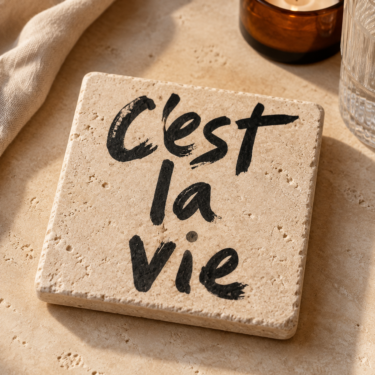 Travertin-Kunstwerk mit schwarzem Schriftzug „C’est la vie“ in einer warmen, sonnenbeschienenen Produktinszenierung
