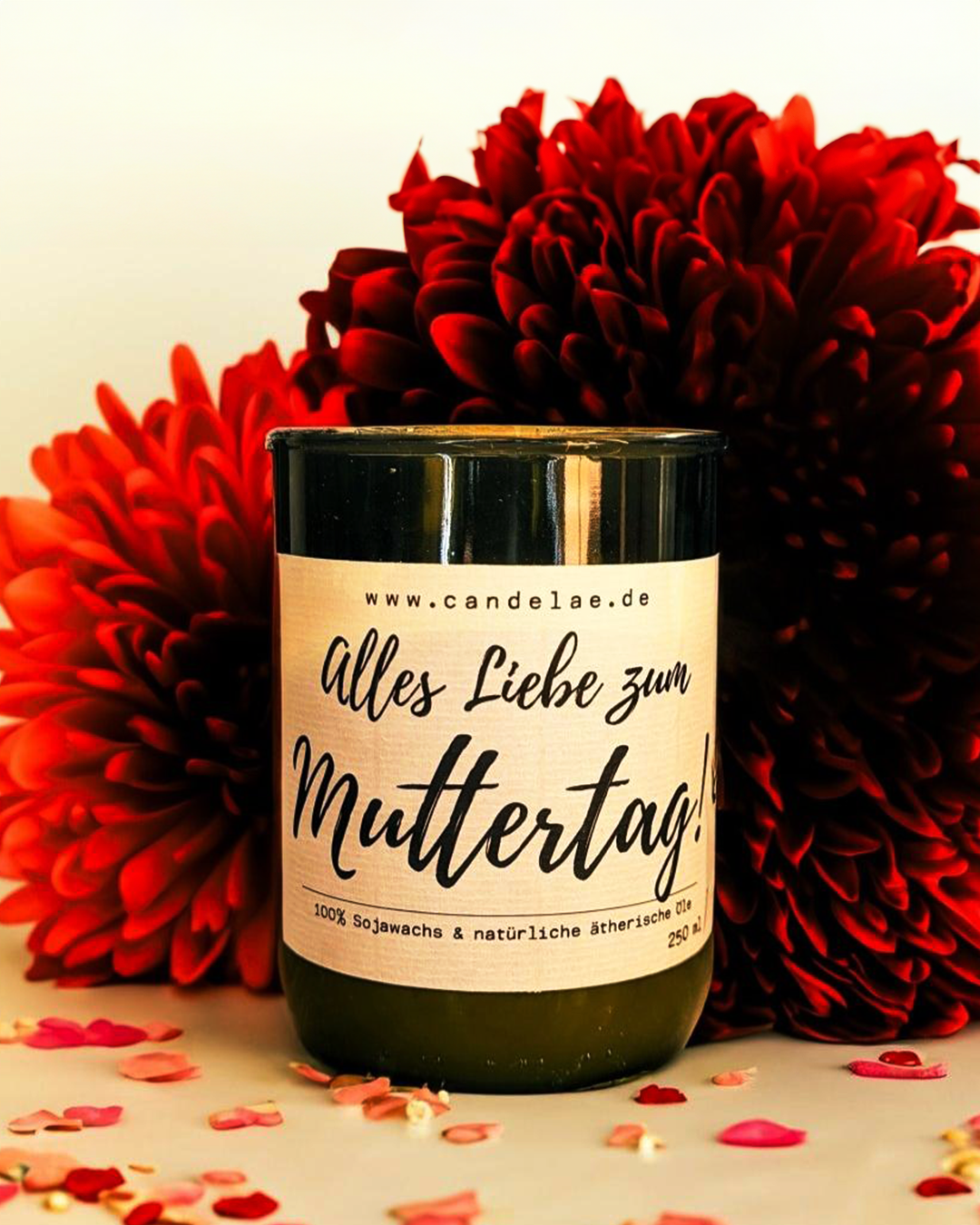 Candelae Duftkerze „Alles Liebe zum Muttertag!“ – Sojawachs mit natürlichen ätherischen Ölen im upgecycelten Weinflaschen-Glas (250 ml); Geschenkidee zum Muttertag mit roten Blüten im Hintergrund.