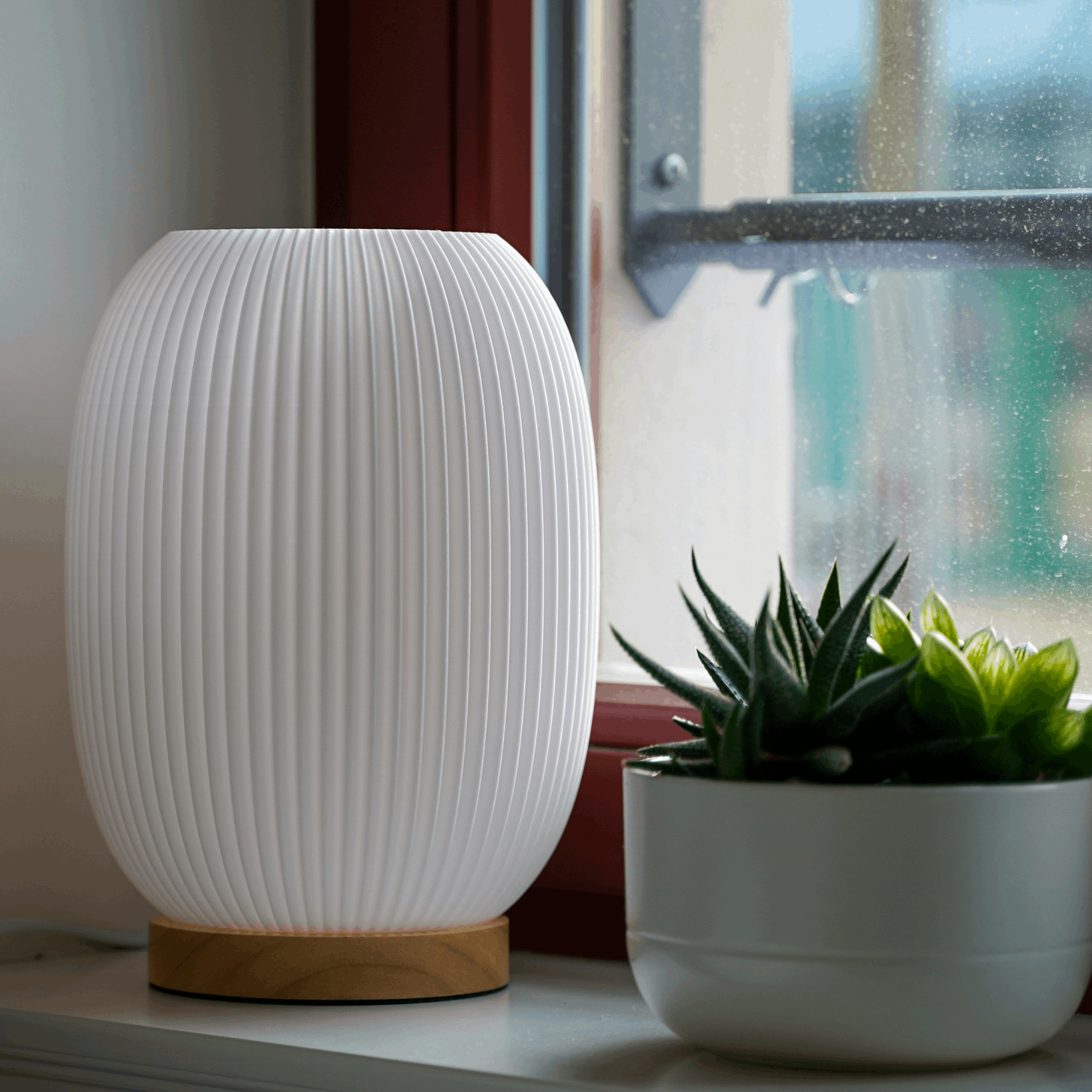 Moonou Boa 3D-gedruckte Tischlampe mit Rillenstruktur und Eichenholz-Sockel, unbeleuchtet am Fenster neben Sukkulente